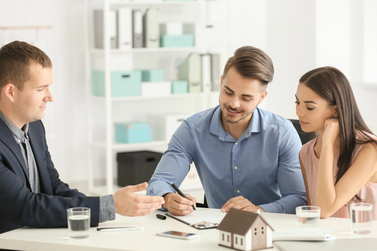 Young man signing a contract for buying house in office of estate agent
