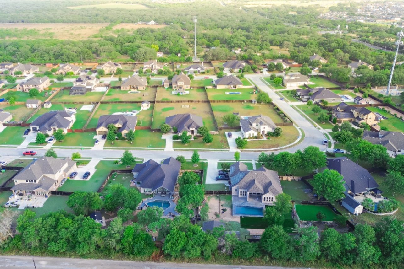 New construction suburban neighborhood and urban sprawl West of San Antonio, Texas, upscale two-story houses on extra big lot acre, swimming pool, solar roofing, lush greenery, aerial view